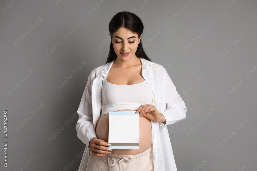 Portrait of beautiful pregnant woman with paper sheet on grey background Portrait of beautiful pregnant woman with paper sheet on grey background