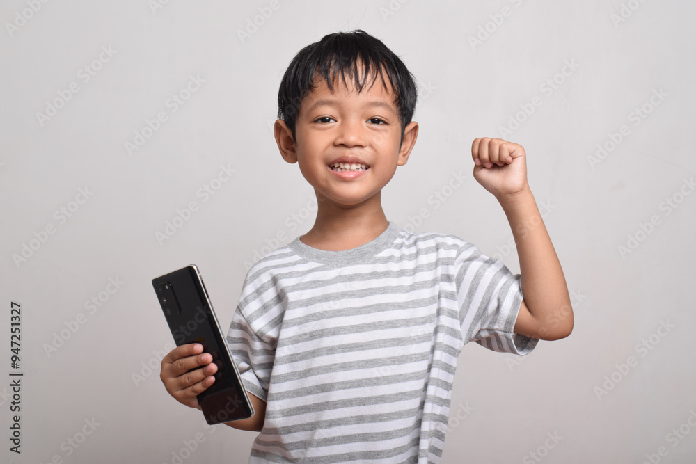 A happy and excited Asian boy with raised hand holding smartphone isolated on white background. little boy holding phone. Technology concept, copy space A happy and excited Asian boy with raised hand holding smartphone isolated on white background. little boy holding phone. Technology concept, copy space