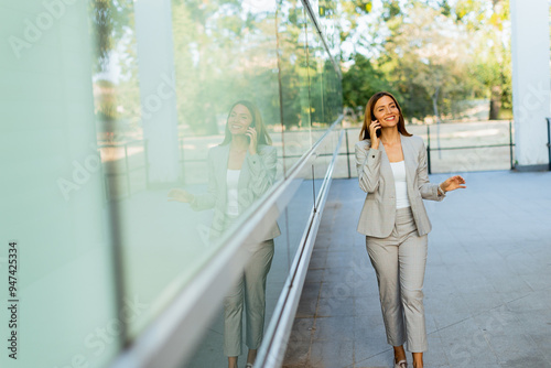 Confident business woman enjoying a sunny day outdoors while browsing her phone near modern architecture surrounded by nature