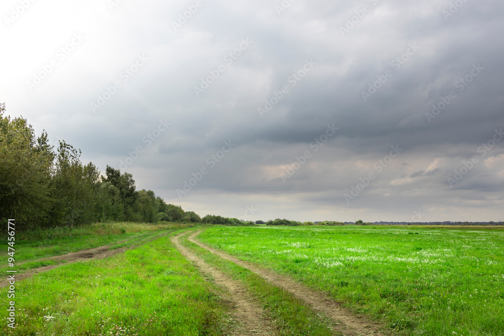 A road cuts through a field of grass on a cloudy day A road cuts through a field of grass on a cloudy day
