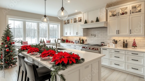 Modern kitchen decorated for Christmas features a white island, bright red Christmas flowers and festive food plates. A green Christmas tree illuminated by natural light. Festive atmosphere.