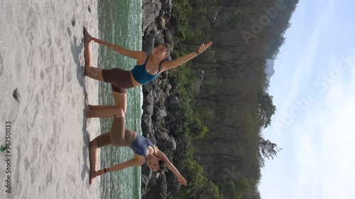 India, Rishikesh. Two young women practice yoga on the beach near the Ganges River. Vertical video.