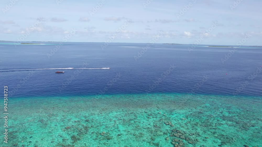 A jet ski floats in the ocean along a green island. Leaving a trail of white waves behind. Dark blue ocean water. Maldives. A green island and a turquoise reef. Top view from a drone. Fast speed