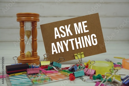 Ask Me Anything text on paper card with hourglass and stationary on wooden background photo