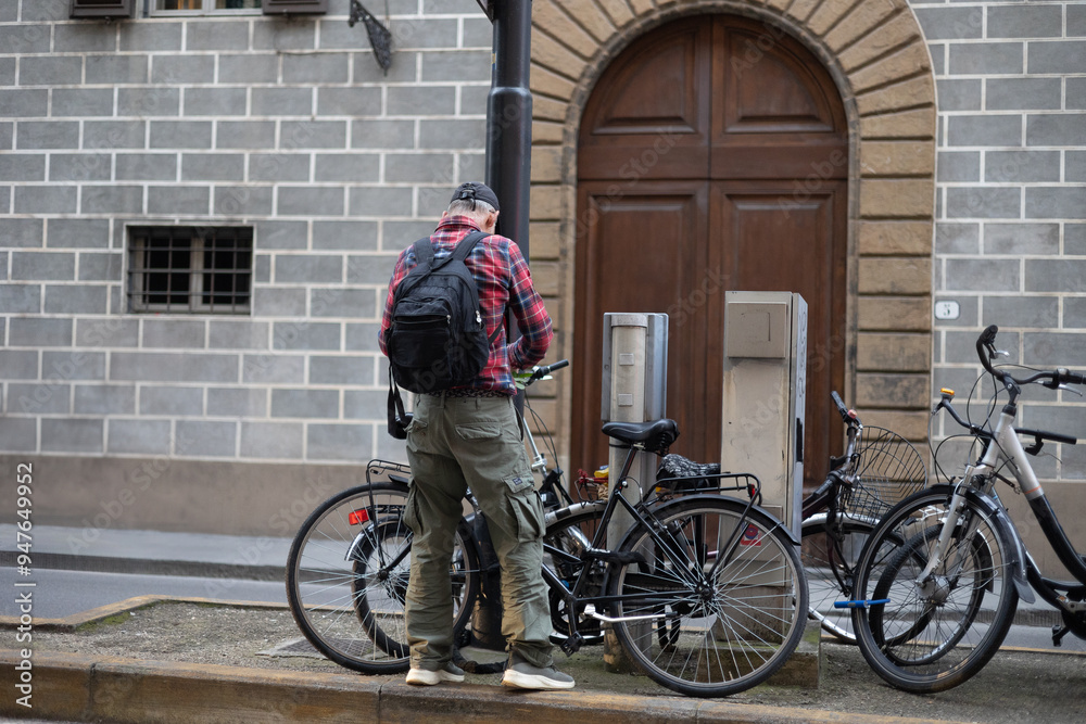 Man with Backpack and Cap Securing his bicycle to a Pole with Hook and Chain Man with Backpack and Cap Securing his bicycle to a Pole with Hook and Chain