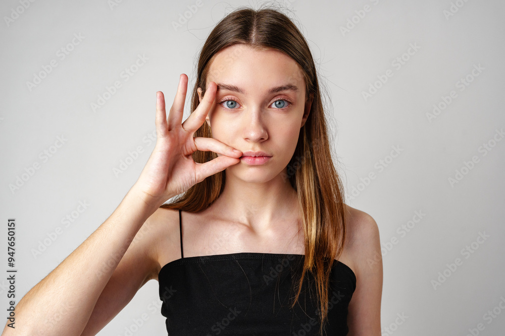 Young Woman With Long Brown Hair Holds Finger to Lips in Studio Portrait Young Woman With Long Brown Hair Holds Finger to Lips in Studio Portrait