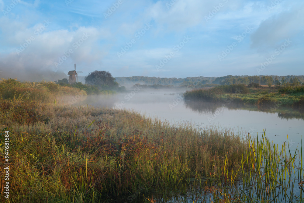 View of an ancient wooden windmill on the banks of the Sorot River on a foggy summer morning, Mikhailovskoye, Pushkinskiye Gory, Pskov region, Russia View of an ancient wooden windmill on the banks of the Sorot River on a foggy summer morning, Mikhailovskoye, Pushkinskiye Gory, Pskov region, Russia