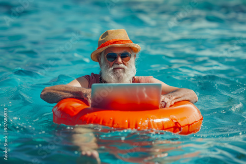 grandfather gentleman senior in sunglasses and a panama hat with laptop swims on a ring in the sea