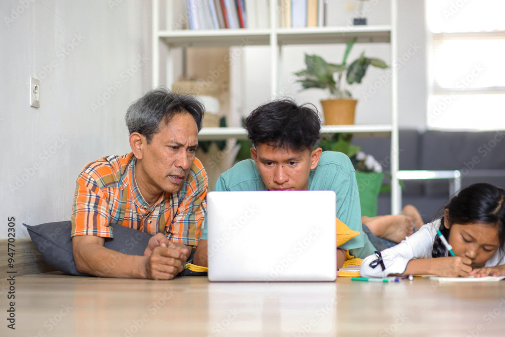 Young Man Doing Homework Using Laptop, Father Telling Son And Daughter Writting On Book Young Man Doing Homework Using Laptop, Father Telling Son And Daughter Writting On Book