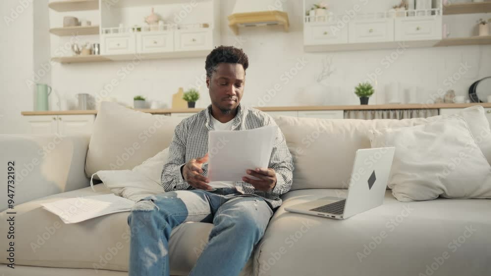 Creative designer or lawyer freelancer working remotely in home office, portrait. Young black man sitting on sofa, viewing papers and typing in work chat in laptop, part-time job online, freelance Creative designer or lawyer freelancer working remotely in home office, portrait. Young black man sitting on sofa, viewing papers and typing in work chat in laptop, part-time job online, freelance