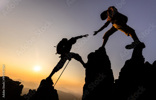 Silhouette of hiker helping each other hike up a mountain at sunset. People helping and, team work concept.