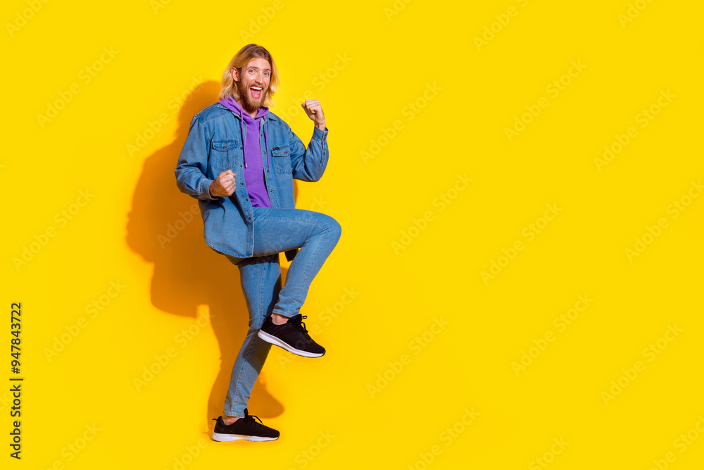 Full length portrait of nice young man raise fists empty space wear denim jacket isolated on yellow color background Full length portrait of nice young man raise fists empty space wear denim jacket isolated on yellow color background