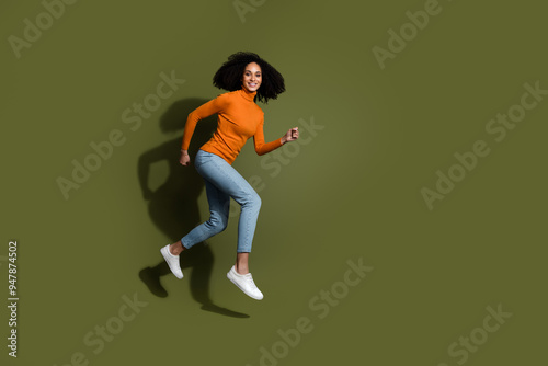 Full length photo of adorable lovely girl wear orange jumper jumping high hurrying empty space isolated khaki color background