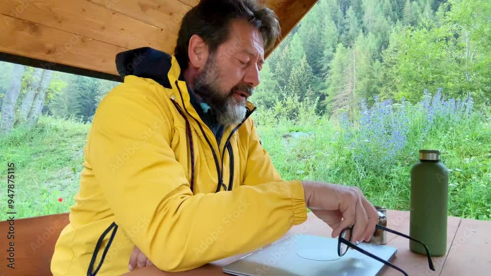 Adult man freelancer traveler wearing yellow jacket anywhere working online using laptop and enjoying nature park mountain around. Modern traveler entrepreneur business lifestyle. Traveling computer Adult man freelancer traveler wearing yellow jacket anywhere working online using laptop and enjoying nature park mountain around. Modern traveler entrepreneur business lifestyle. Traveling computer