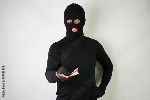 Dangerous young Adult black masked robber is holding a bunch of indonesian money after stealing from his victim.