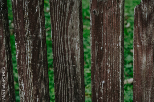 Weathered wooden fence panels standing between lush green grass on a sunny day in a tranquil outdoor setting photo