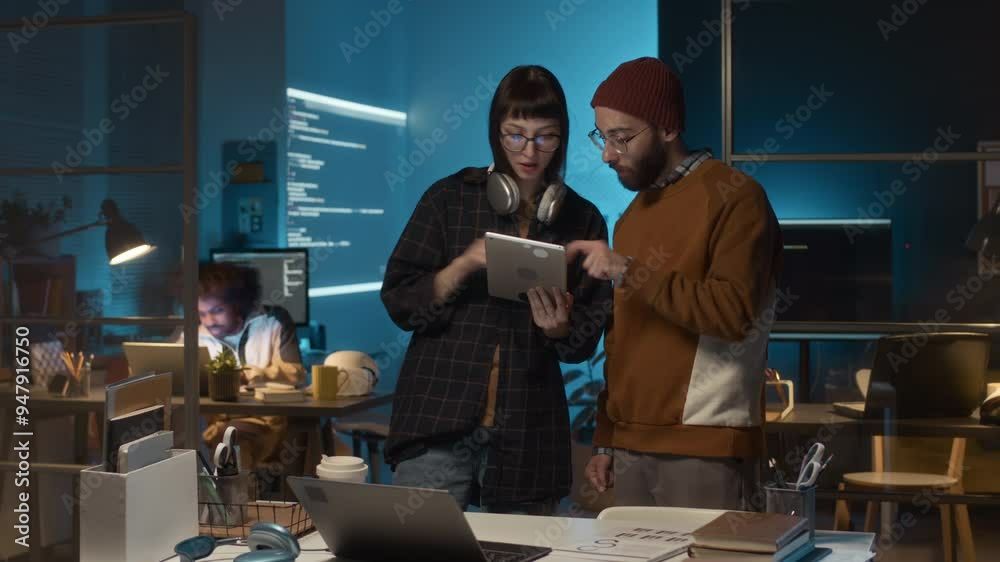 Timelapse shot of group of diverse IT support specialists looking at tablet and having conversation about software applications while working on project under deadline during nightime Timelapse shot of group of diverse IT support specialists looking at tablet and having conversation about software applications while working on project under deadline during nightime