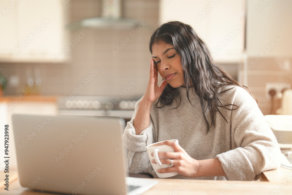 A Woman Experiencing Stress While Working on a Laptop at Her Kitchen Table in the Morning Light A Woman Experiencing Stress While Working on a Laptop at Her Kitchen Table in the Morning Light