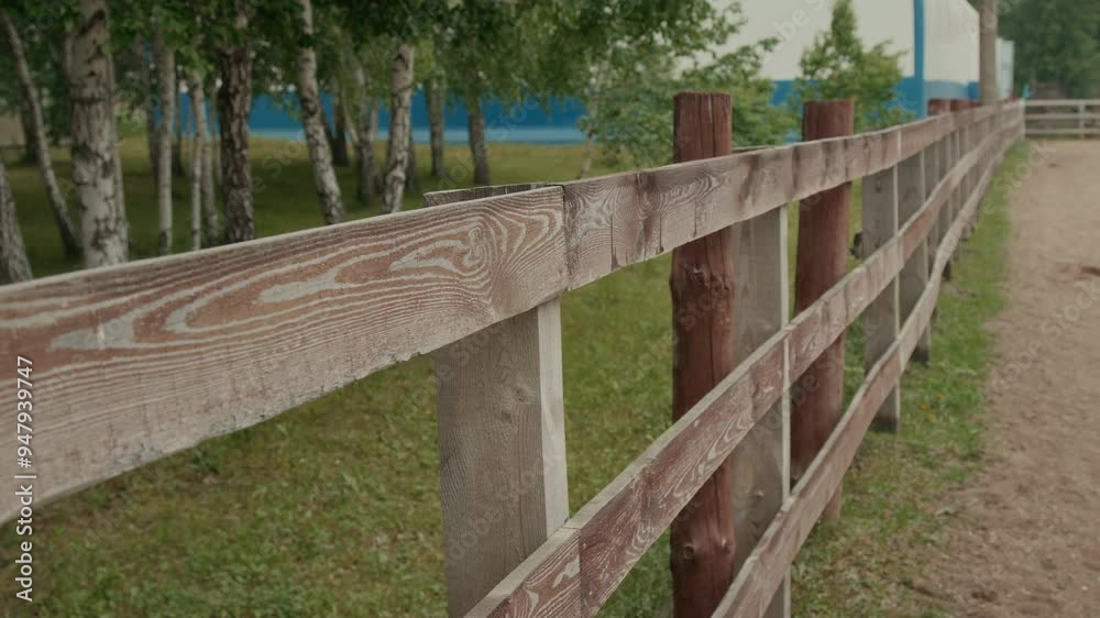 Weathered wooden stable fence built with hick horizontal planks and sturdy posts, stretching across a quiet, empty outdoor horse riding practice arena with no people Weathered wooden stable fence built with hick horizontal planks and sturdy posts, stretching across a quiet, empty outdoor horse riding practice arena with no people