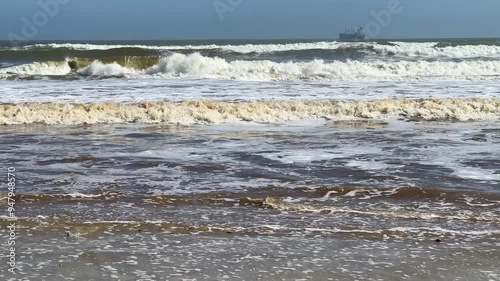 White surf with a cargo ship on the horizon photo