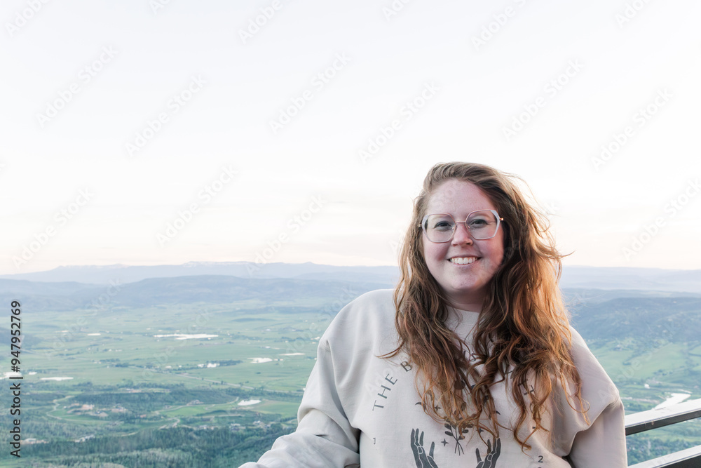 Smiling woman with glasses standing before a vast scenic valley view Smiling woman with glasses standing before a vast scenic valley view
