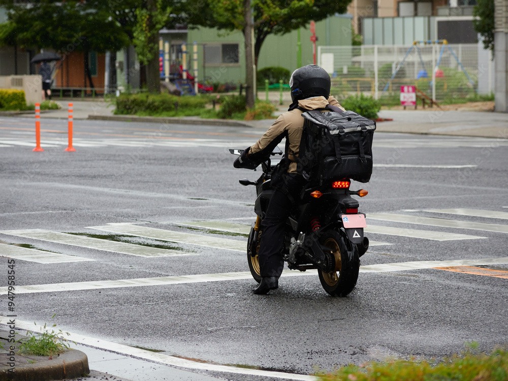 Obraz premium 夏の雨の日の都市の道路の交差点で信号待ちの出前のオートバイ運転手の姿