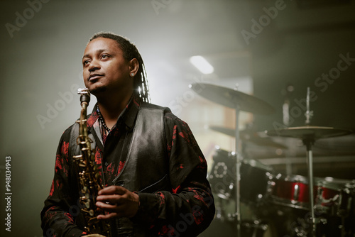 Canvas Print Medium shot of African American male jazz musician holding saxophone standing on