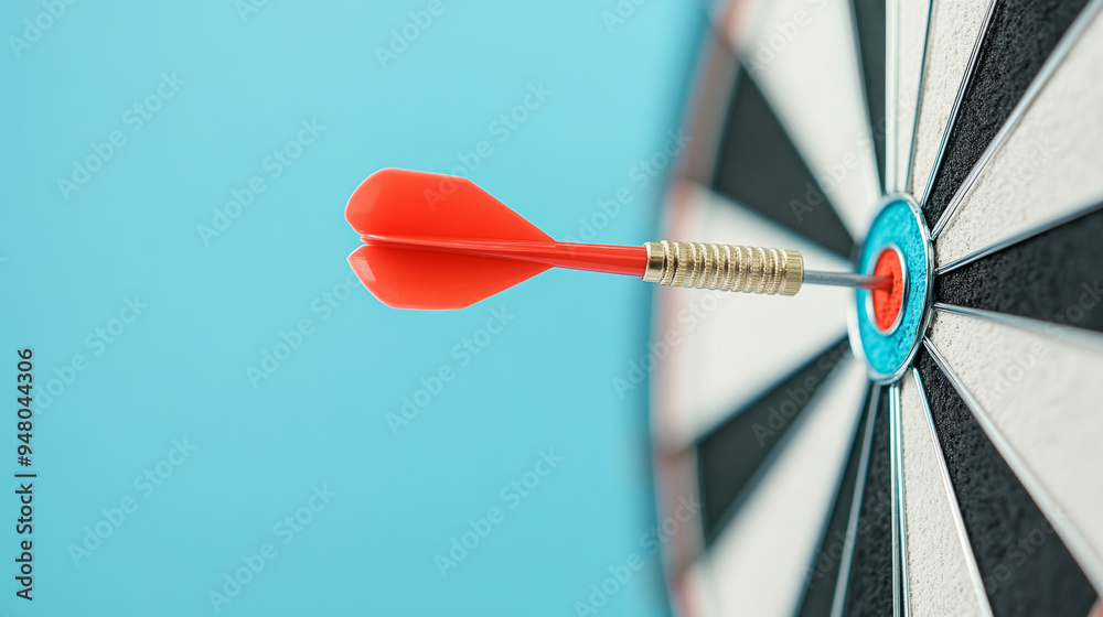 a dart hitting the bullseye on a dartboard with a clear blue sky background. The red dart contrasts with the black and white rings of the dartboard a dart hitting the bullseye on a dartboard with a clear blue sky background. The red dart contrasts with the black and white rings of the dartboard