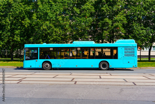 Blue bus side view on the road in city green trees street