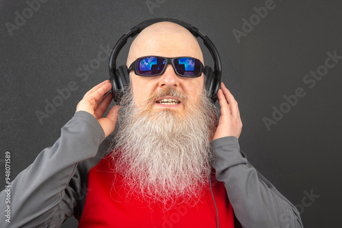 portrait of a man wearing sunglasses and a large white beard with headphones on his head, relaxing and listening to music photo