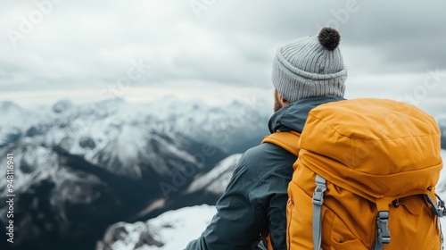 A backpacker dressed in hiking gear and a gray beanie overlooks a stunning snowy mountainous landscape, embodying adventure and solitude.