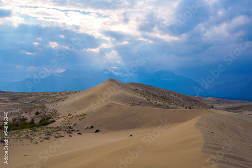 Sunlit desert dunes under a dramatic cloudy sky