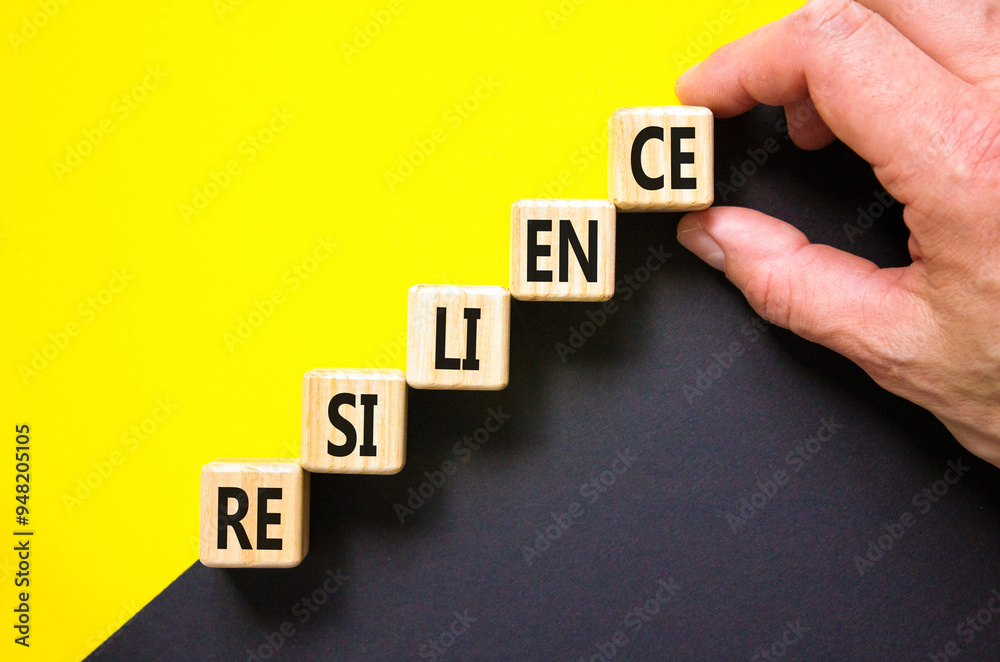 Obraz premium Resilience symbol. Concept word Resilience on beautiful wooden cubes. Beautiful yellow and black background. Businessman hand. Business resilience concept. Copy space.