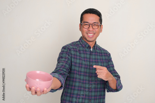 A man smiling happy and pointing at empty dinning bowl that he hold photo