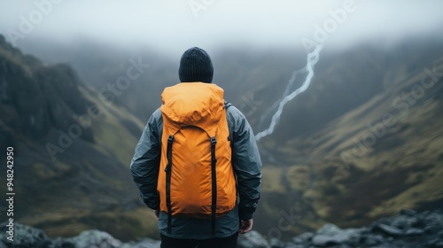 This image depicts a hiker with an orange backpack facing a majestic mountain range, capturing the sense of adventure, exploration, and connection with nature in a dramatic landscape.