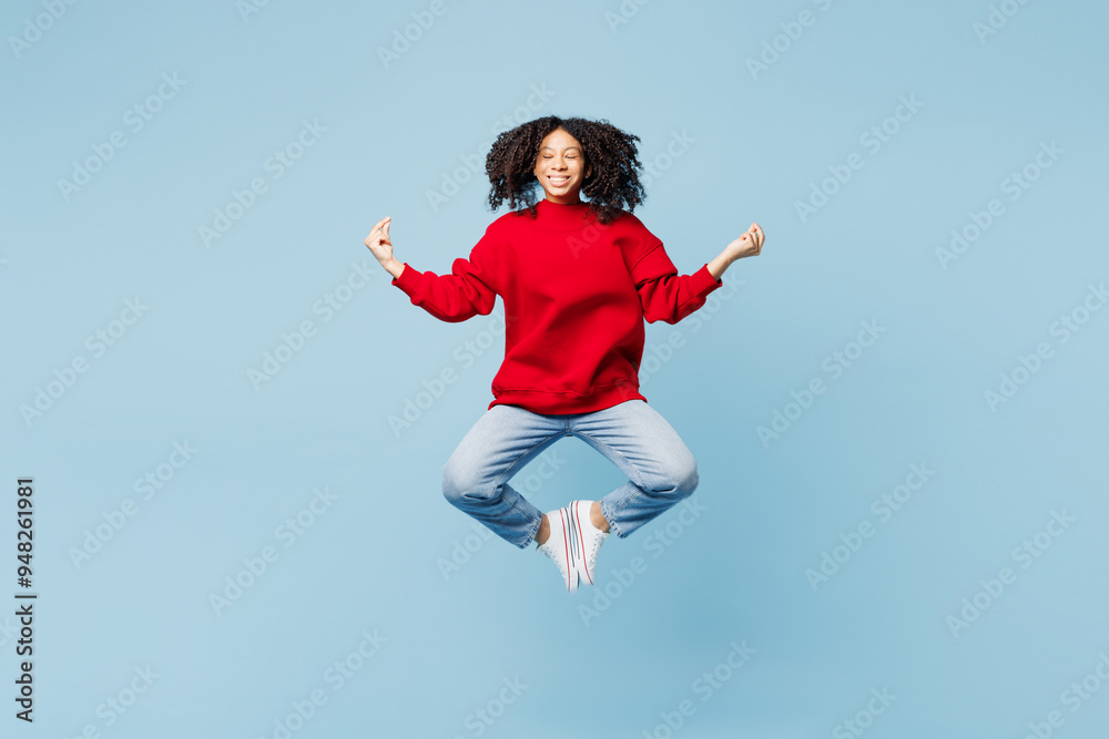 Full body little kid teen girl of African American ethnicity wear red sweatshirt jump high hold hands arms in yoga om aum gesture relax isolated on plain blue background. Childhood lifestyle concept. Full body little kid teen girl of African American ethnicity wear red sweatshirt jump high hold hands arms in yoga om aum gesture relax isolated on plain blue background. Childhood lifestyle concept.