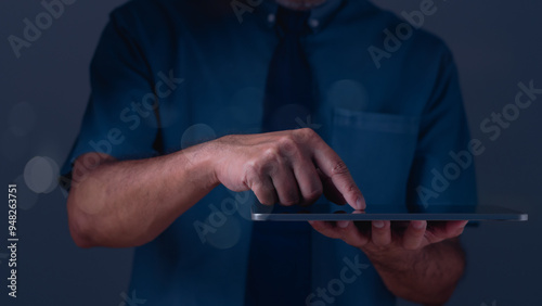 A man wearing a blue shirt and a tie is holding a tablet in his hand. He is pointing at something on the screen, possibly indicating a message or an app. Concept of modern technology