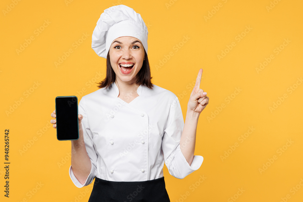 Young surprised chef cook baker woman wear white shirt black apron uniform toque chefs hat hold use blank screen area mobile cell phone isolated on plain yellow background studio Cooking food concept Young surprised chef cook baker woman wear white shirt black apron uniform toque chefs hat hold use blank screen area mobile cell phone isolated on plain yellow background studio Cooking food concept