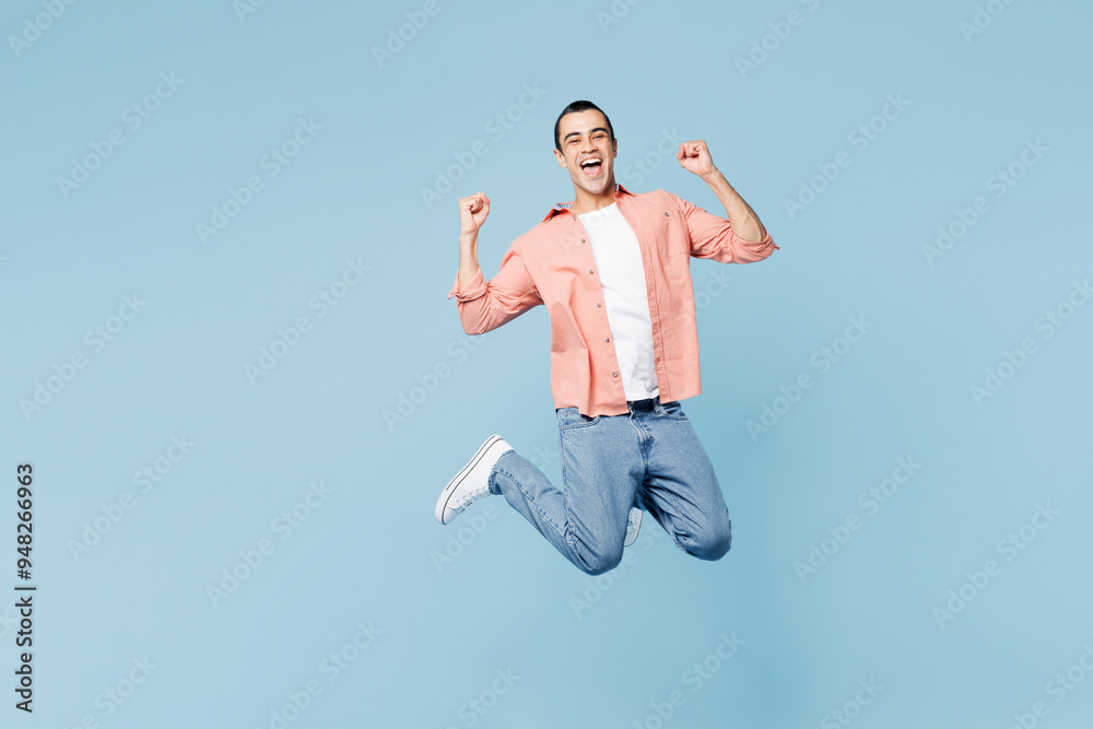 Full body young cool middle eastern man he wear pink shirt white t-shirt jump high do winner gesture clench fist isolated on plain pastel light blue cyan background studio portrait. Lifestyle concept. Full body young cool middle eastern man he wear pink shirt white t-shirt jump high do winner gesture clench fist isolated on plain pastel light blue cyan background studio portrait. Lifestyle concept.
