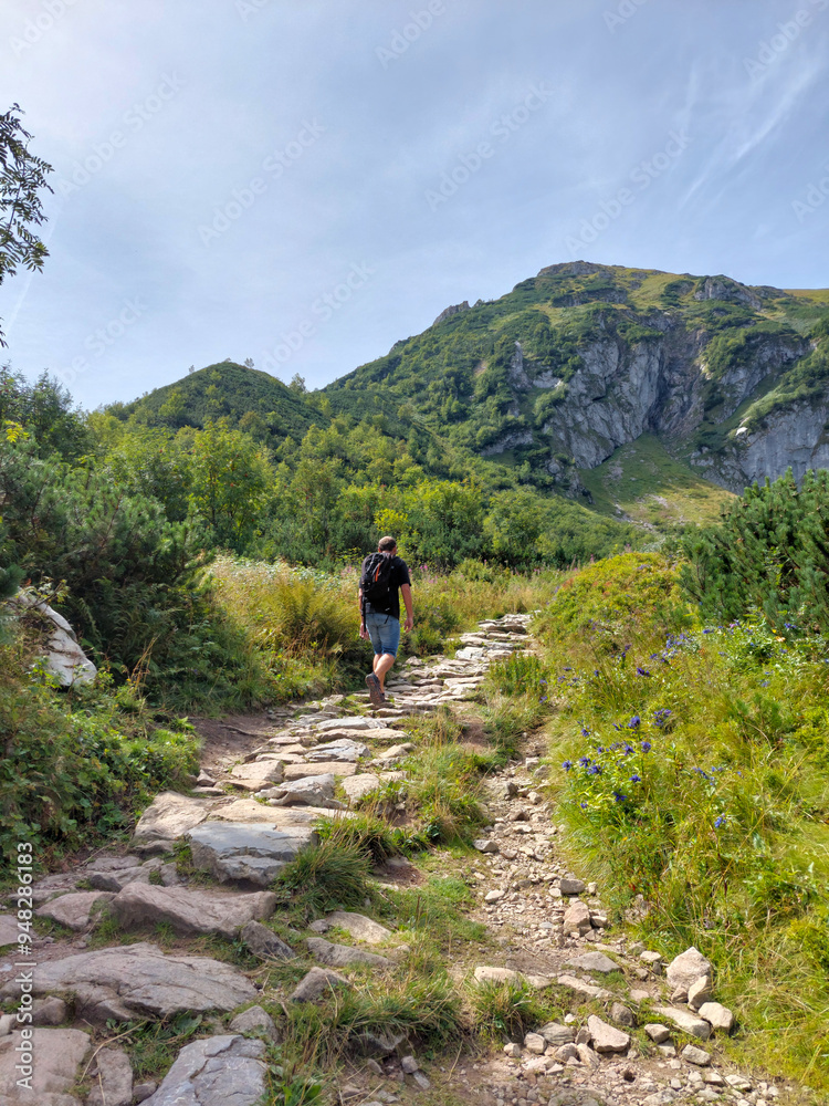 Obraz premium Tourist is enjoying a summer hike on a rocky trail leading to the summit of giewont mountain