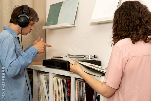 Man listens to vinyl record using headphones, woman chooses records.