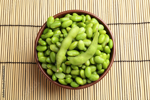 Raw green edamame soybeans and pods on wicker mat, top view photo