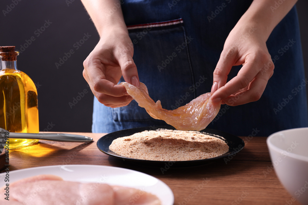Making schnitzel. Woman coating slice of meat with bread crumbs at wooden table, closeup Making schnitzel. Woman coating slice of meat with bread crumbs at wooden table, closeup