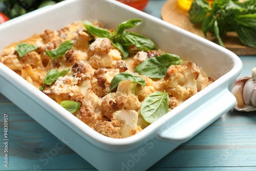 Tasty baked cauliflower and basil in baking dish on light blue wooden table, closeup