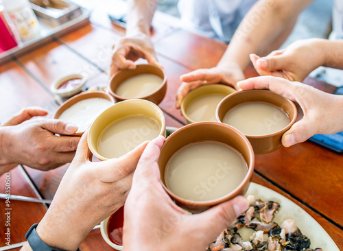 Udo Island, Jeju-si, Jeju-do, South Korea - July 16, 2021: Close-up of hands for toast with Makgeolli(unrefined rice wine) on glass at a sushi restaurant photo