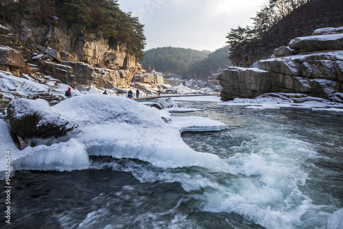 Cheorwon-gun, Gangwon-do, South Korea - January 2, 2022: Winter view of snow covered canyon with ice and water with tourists walking on deck trail on Hantangang River photo