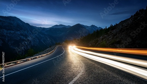 Dramatic long exposure of a mountain road at night with car headlights illuminating the way.