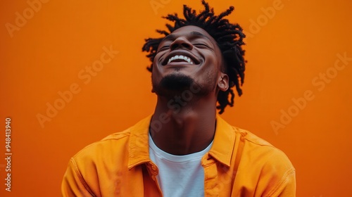 A man wearing an orange jacket and white t-shirt stands against a vibrant orange background, creating a striking and vivid visual contrast with his attire.