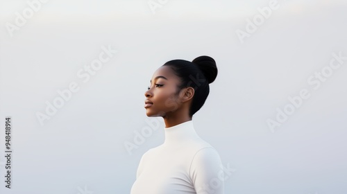 Side profile of a young African woman with her hair in a bun, wearing a white high-neck top against a light background.