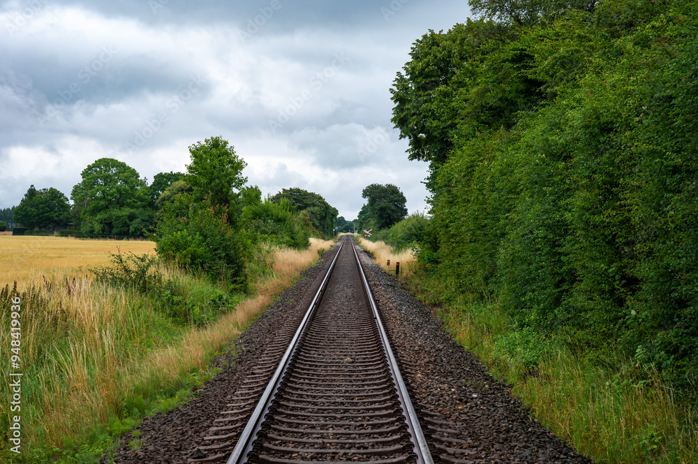 Fototapeta premium Sakskobing, Lolland, Denmark, July 22, 2024 - Straight railroad track through the fields at the Danish countryside